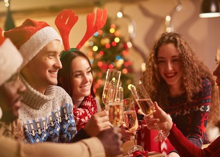 People in Christmas sweaters cheering champagne.